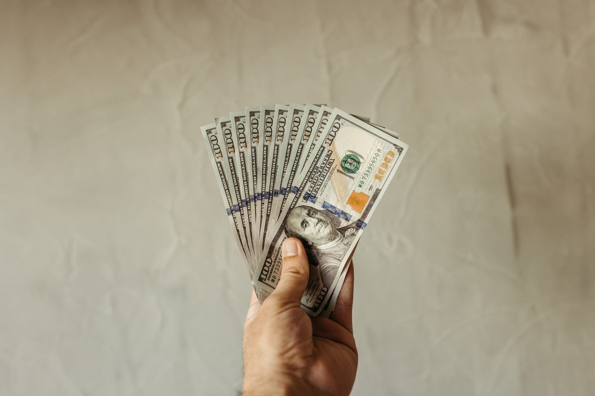 A close-up of a hand holding multiple US dollar bills