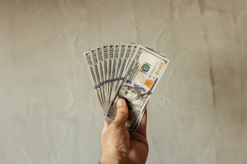 A close-up of a hand holding multiple US dollar bills