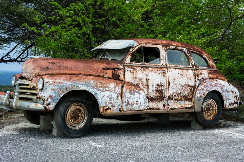 A heavily rusted vintage car abandoned outdoors, surrounded by nature