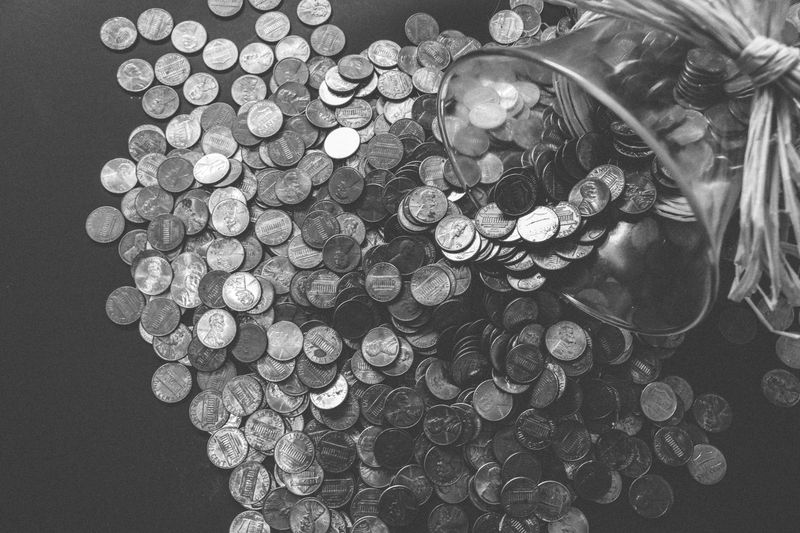 Monochrome image of coins spilling from a glass jar