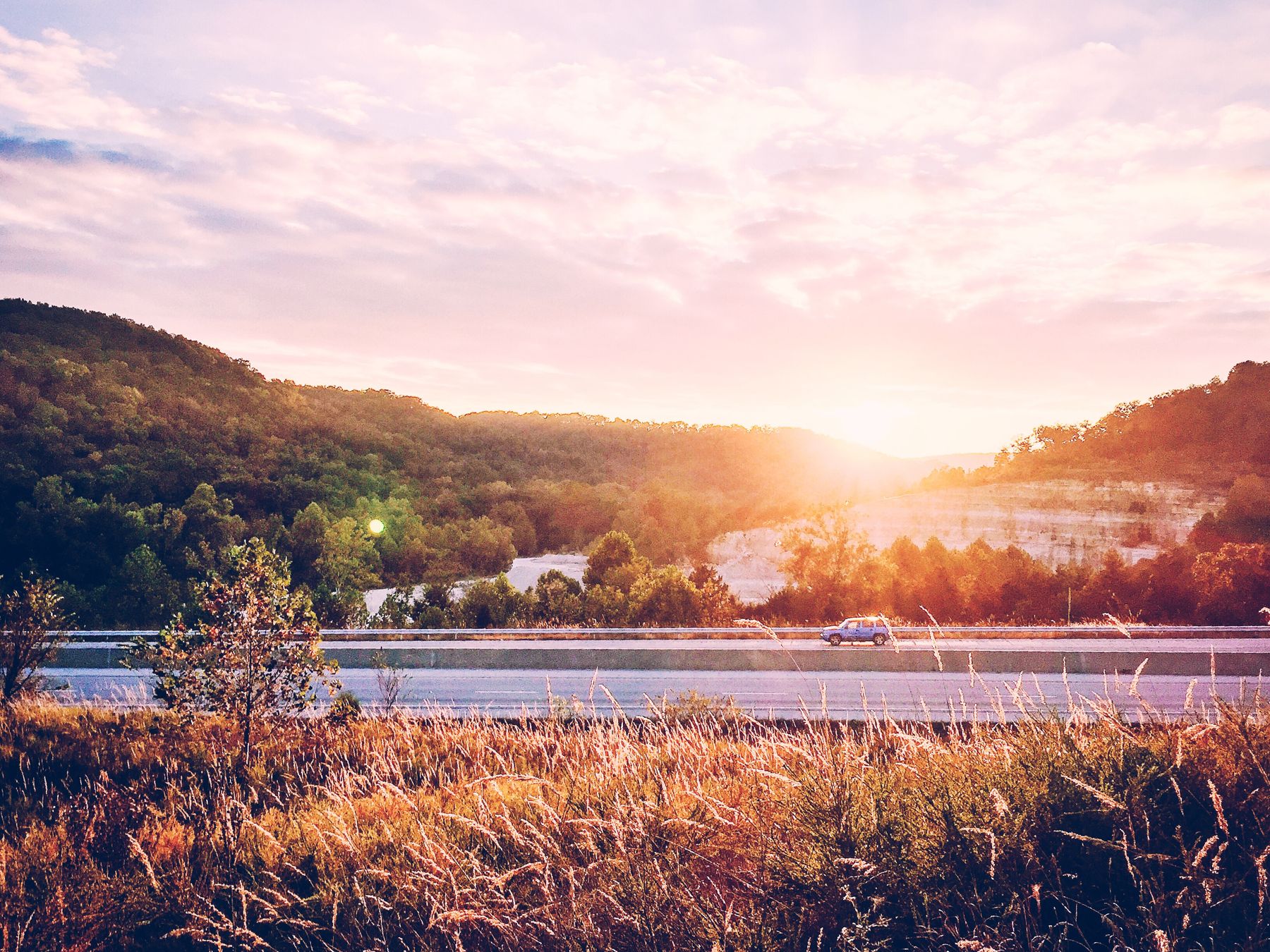 A serene highway scene at sunrise, with trees and hills