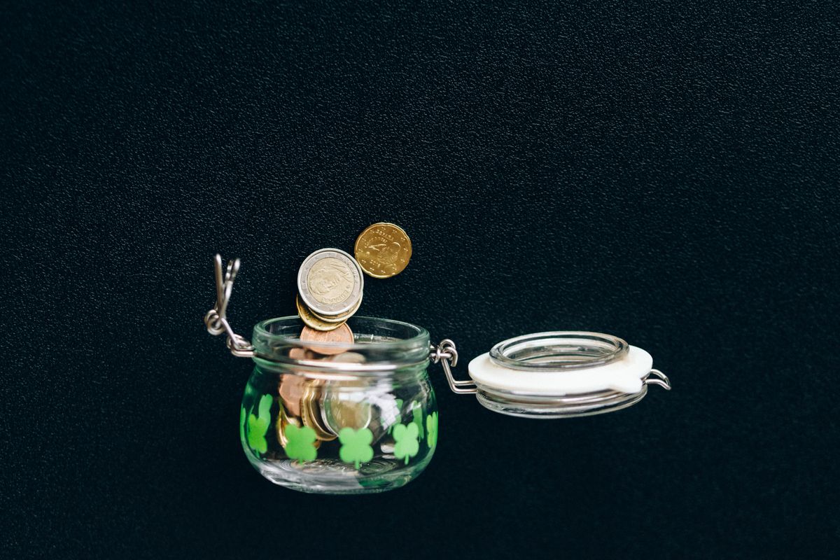 Glass jar with coins falling into it on a black background