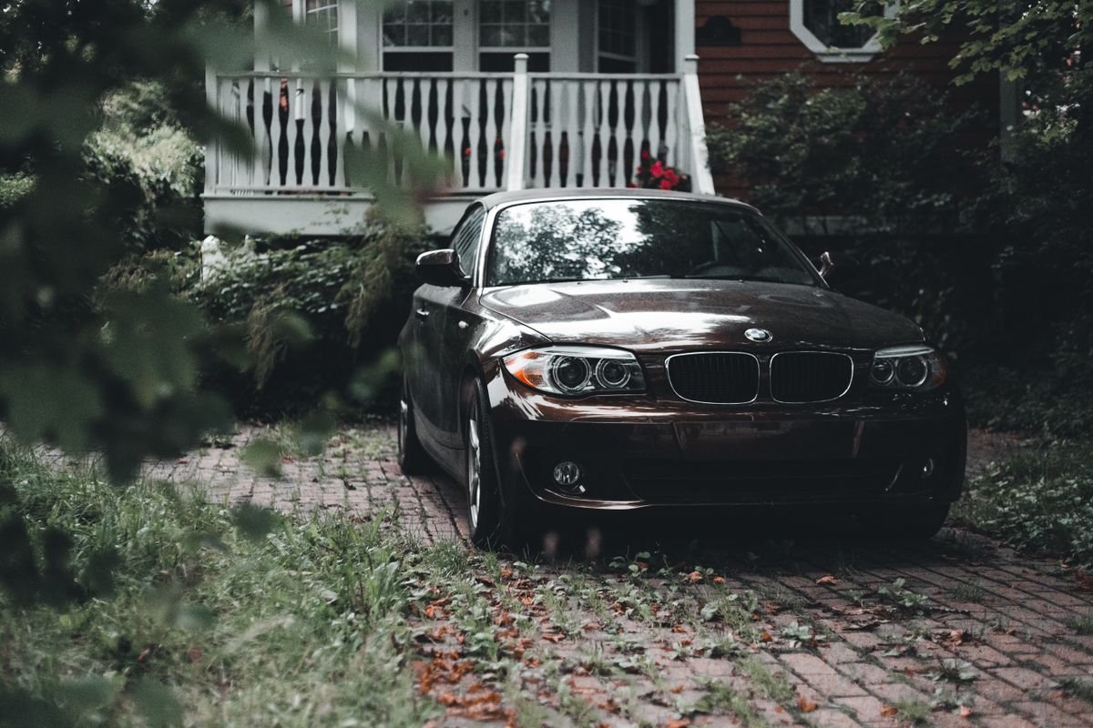 Black sedan parked on paved path amidst greenery and a wooden veranda